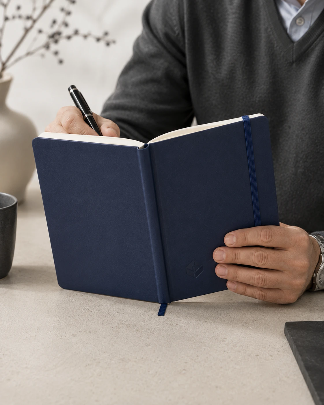 Person writing in a navy branded notebook