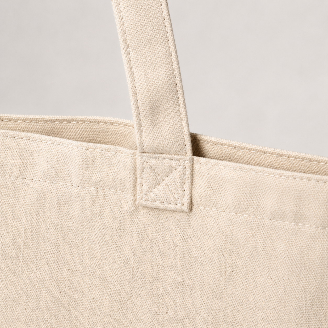 Close-up of natural cotton canvas texture, top hem stitching and reinforced tote handle attachment