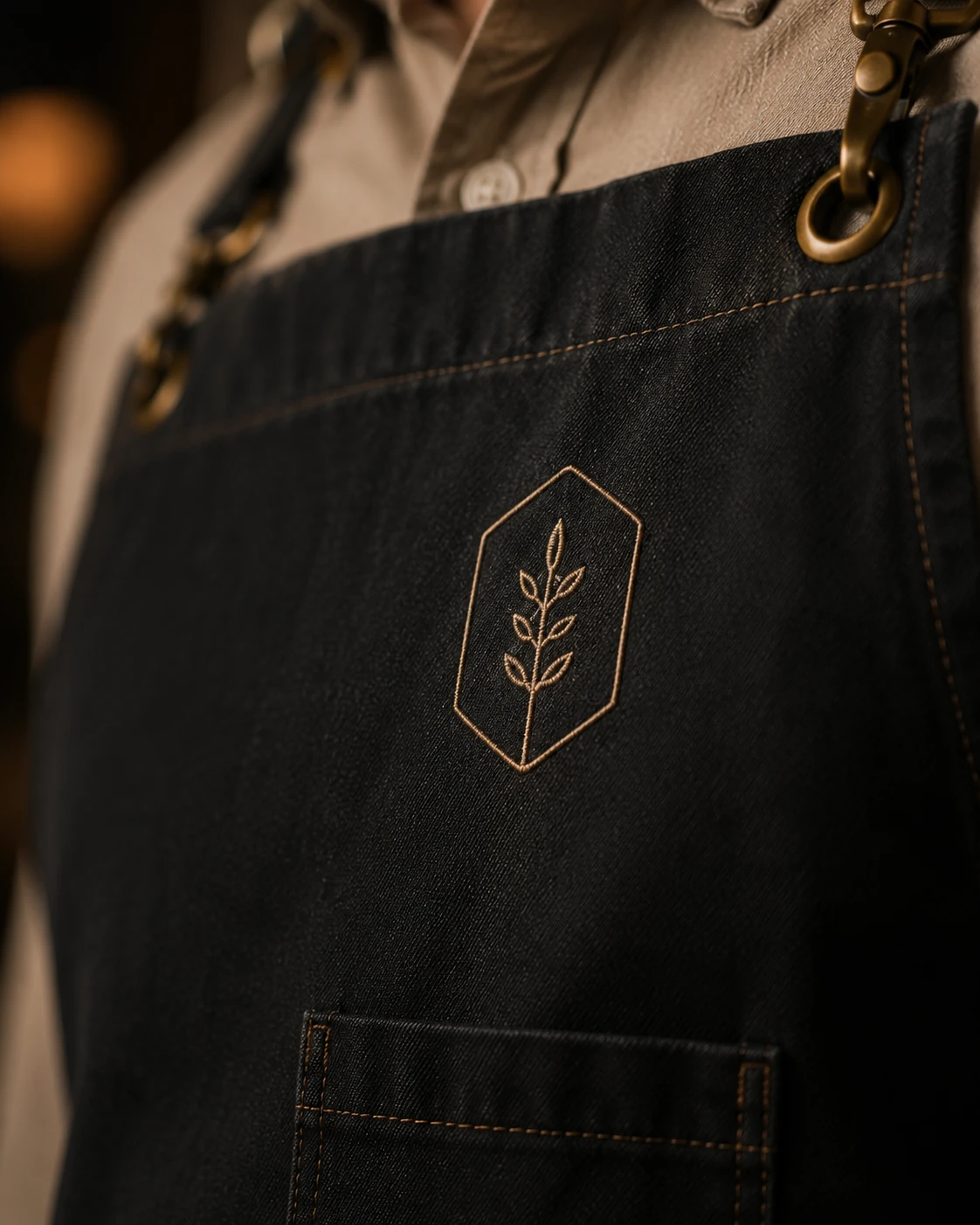 Close-up of an embroidered botanical emblem on a dark bib apron